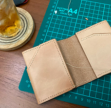 A hand-stitched leather card wallet on a cutting mat.
