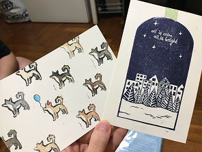 Two linocut prints: a repeating pattern of dogs, and a night-time cityscape under the stars.