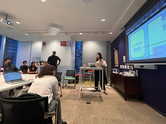 A presenter sharing ideas on a large screen with stakeholders seated around a meeting room.
